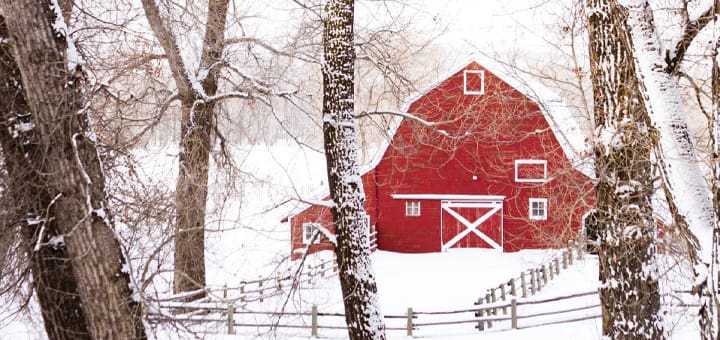 Red barn in a snow-covered landscape with bare trees.