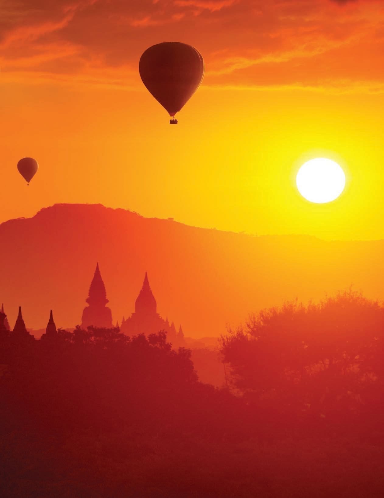 Two hot air balloons float in the sky over pagodas at sunset.