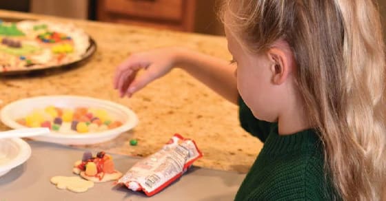 A young child decorates a cookie with colorful candies.