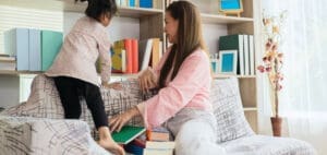 Woman and child interacting near a bookshelf and couch.