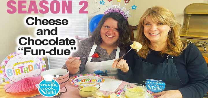 Two people in aprons holding fondue forks at a table with a birthday sign and snacks.