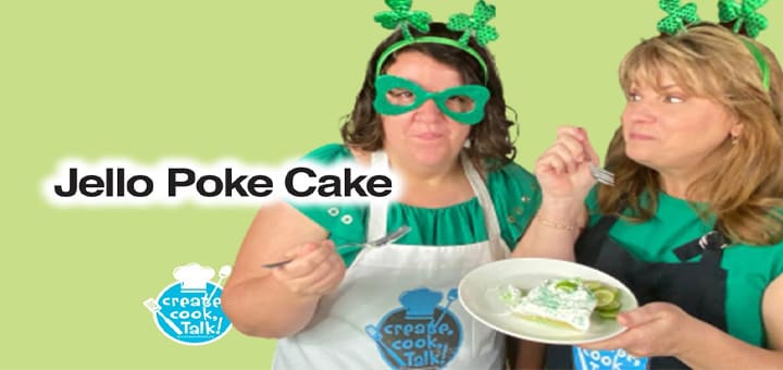 Two women wearing St. Patrick's Day accessories present a slice of Jello poke cake.