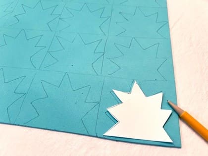 A blue sheet of craft foam with zig-zag shapes drawn on it and one white star shape cut out, next to a pencil.