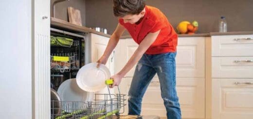 Boy in red shirt and jeans loading plates into dishwasher