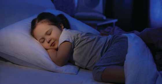 A young child sleeps peacefully on a pillow in a dimly lit room.