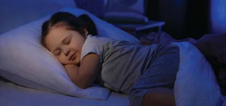 A young child sleeps soundly on a pillow in a dimly lit room.