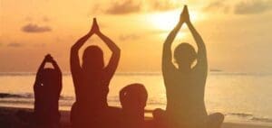 Silhouettes of people meditating on a beach at sunset.
