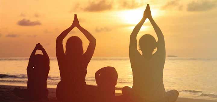 Silhouettes of people meditating on a beach at sunset.