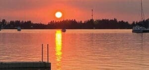Sunset over the water with a dock in the foreground and boats in the distance.
