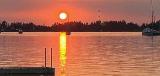 Sunset over the water with a dock in the foreground and boats in the distance.