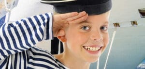 Young boy in a sailor uniform salutes and smiles.