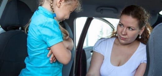 A child with arms crossed looks away from a woman inside a car.
