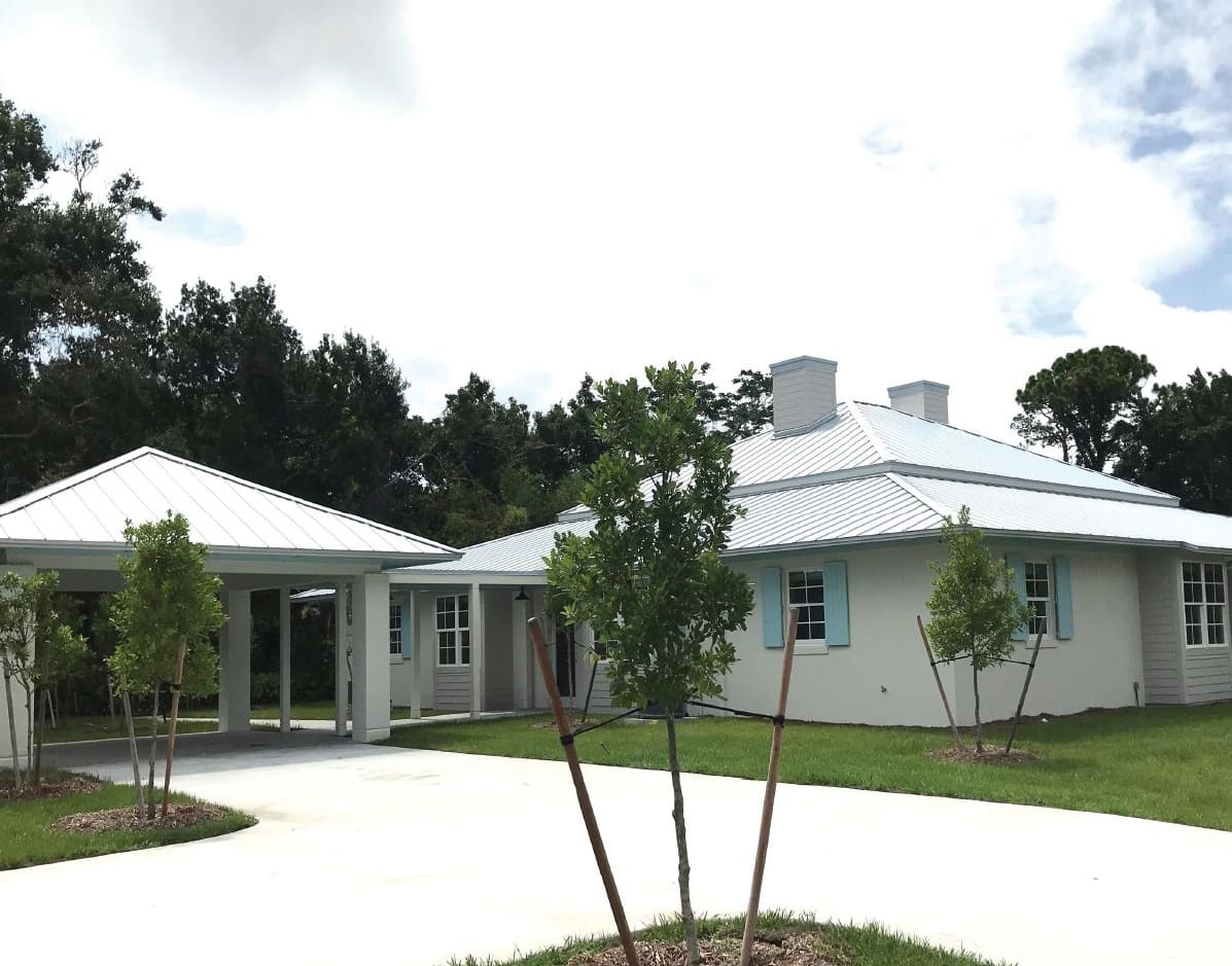 White house with a carport and trees in front.