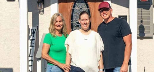 Three people stand smiling in front of a house.