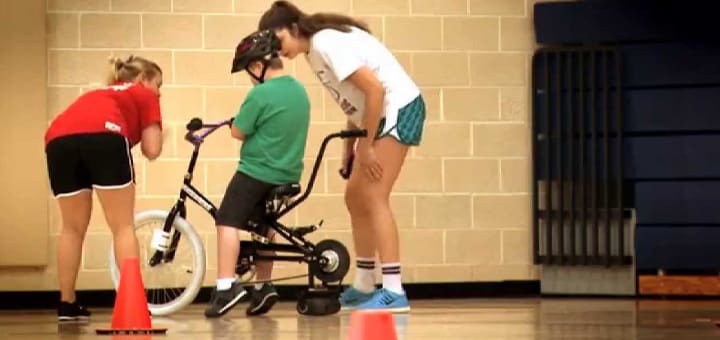 Three people in a gym with a person on a bicycle.