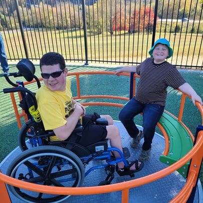 Two children enjoy an inclusive playground merry-go-round.