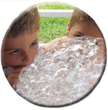 Two children lean in to blow bubbles.