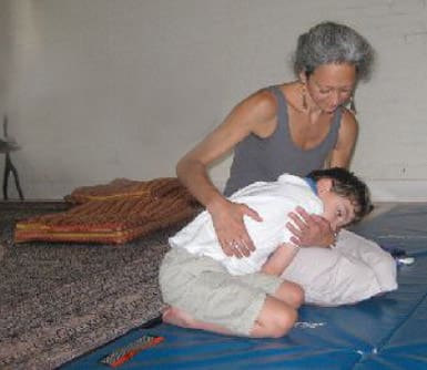 A mother comforting her son, Andreas, on a floor mat during a therapy session.