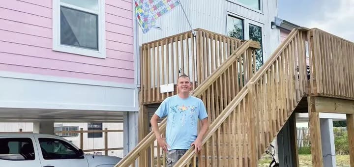 Man standing on wooden stairs in front of a pink house.
