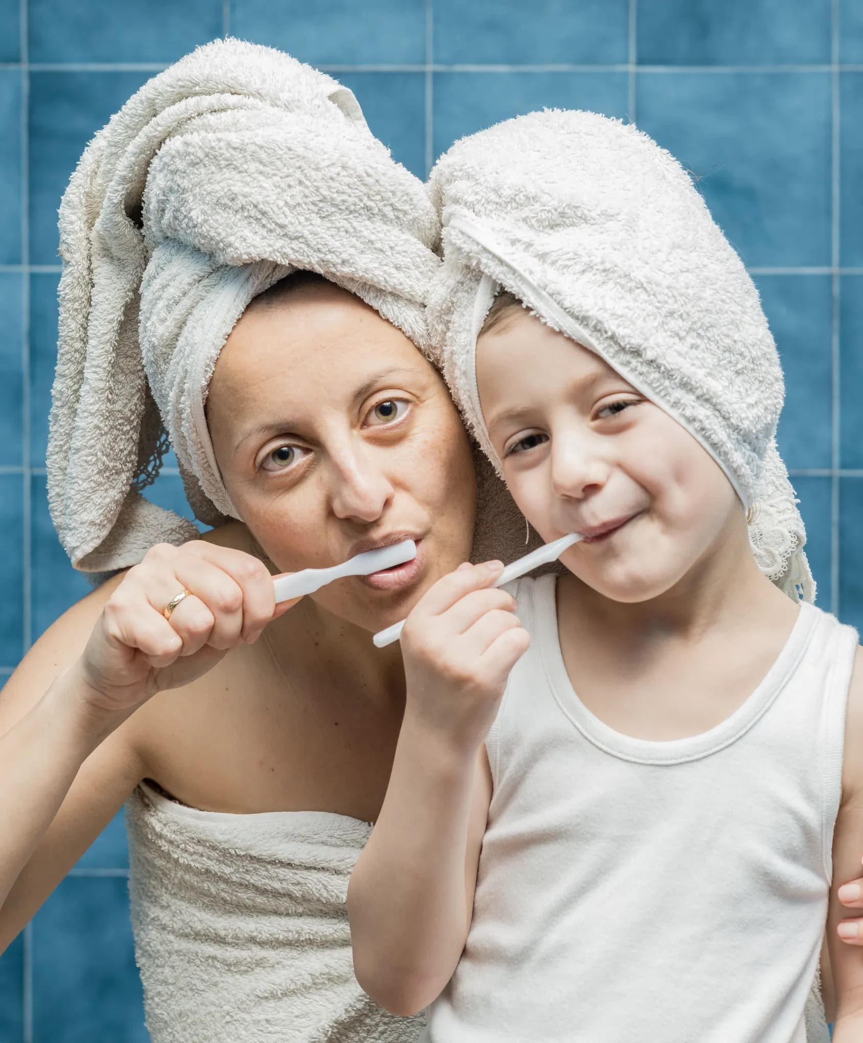 Woman and child brushing teeth with towels on their heads