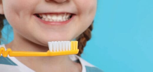 Child smiling with toothbrush in front of mouth against a blue background.
