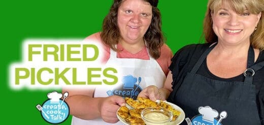 Two women holding a plate of fried pickles with dipping sauce.