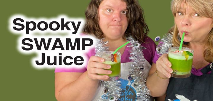 Two women drink green spooky swamp juice from glasses with straws.