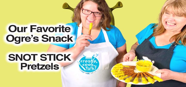 Two women in aprons hold a plate of pretzels and a yellow utensil with text about "Ogre's Snack SNOT STICK Pretzels.