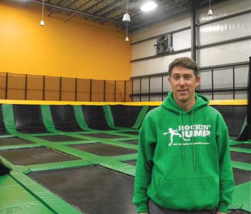 Man in a green Rockin' Jump hoodie standing in a trampoline park.