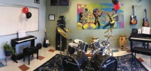 Music room with instruments, including a drum set, keyboard, guitars, and congas, plus a colorful mural on the wall.