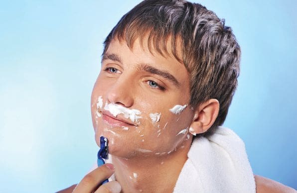 Young man with shaving cream on his face holds a razor.