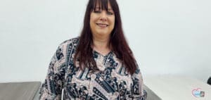 Woman with dark hair and bangs, wearing a patterned blouse, smiles.