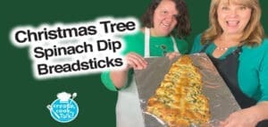 Two women holding a Christmas tree-shaped spinach dip breadstick.