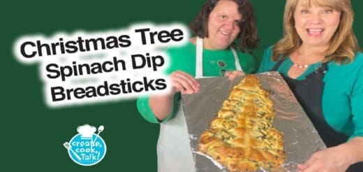 Two women holding a Christmas tree-shaped spinach dip breadstick.