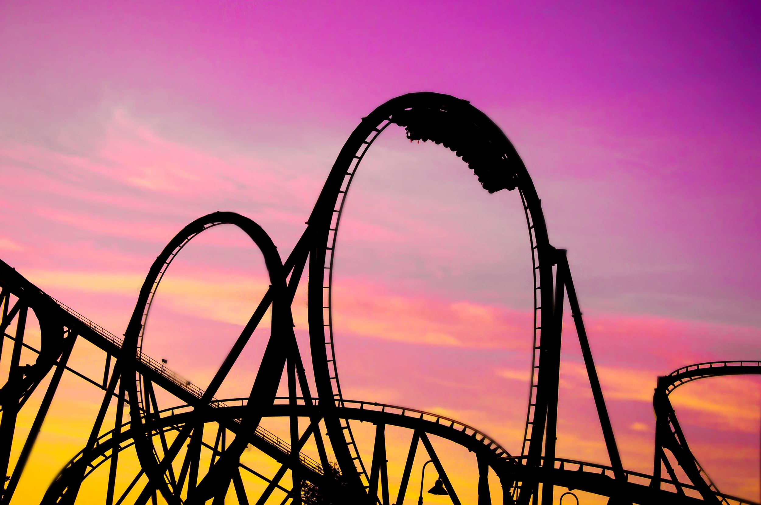 Silhouette of a roller coaster against a purple and orange sunset sky.