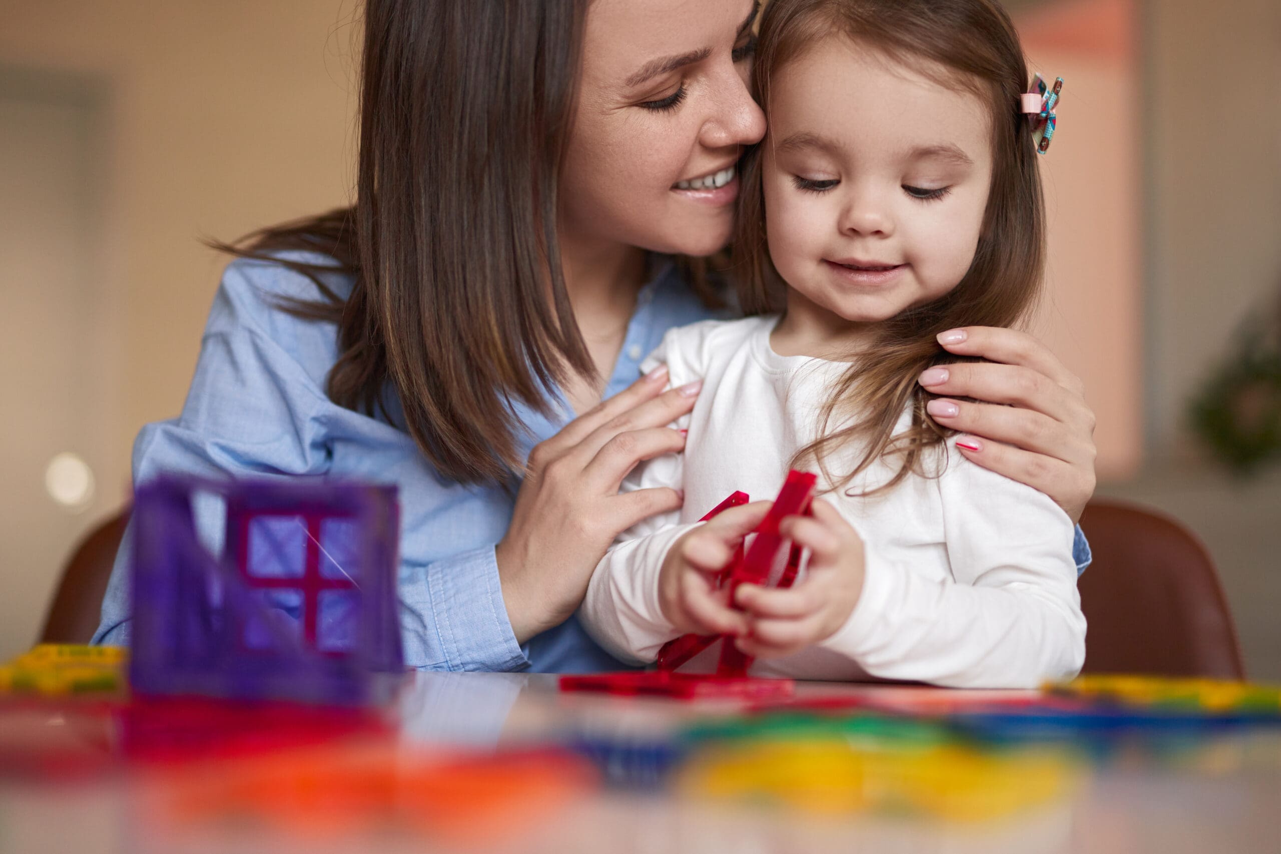Mother and daughter building with colorful magnetic shapes together at a table.