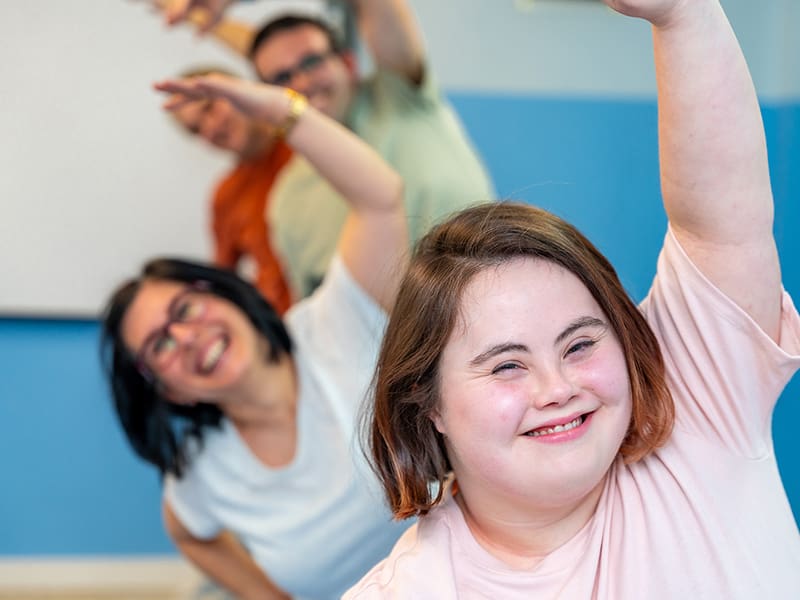 A group of people with Down syndrome doing yoga stretches indoors.
