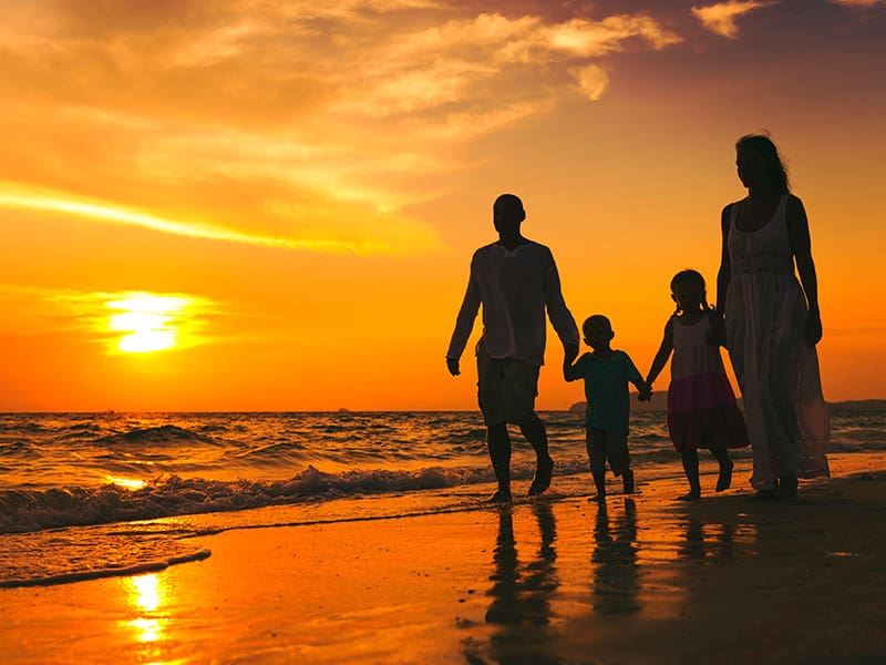 Silhouetted family walking on a beach at sunset.