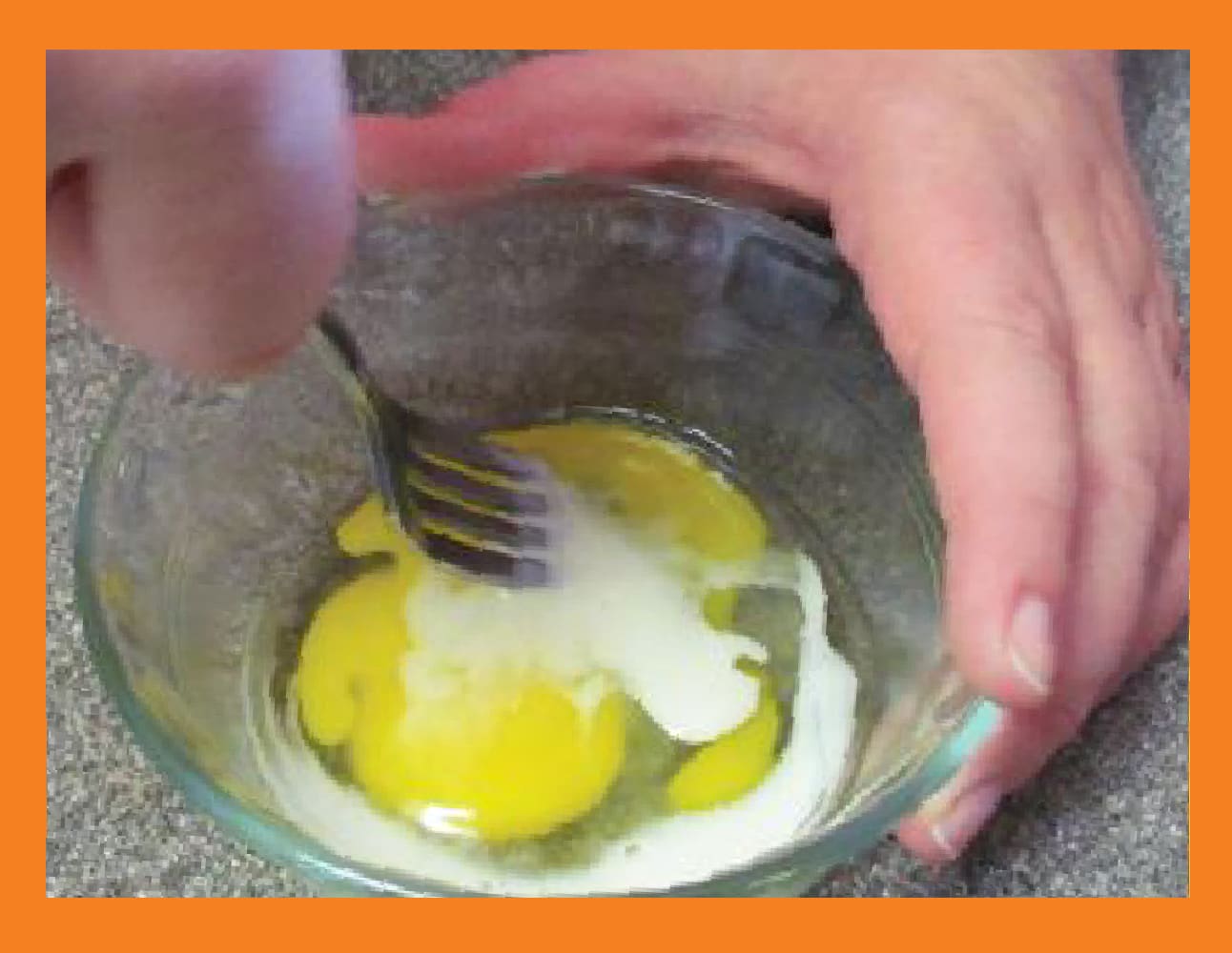 A fork stirs eggs and milk in a clear bowl.