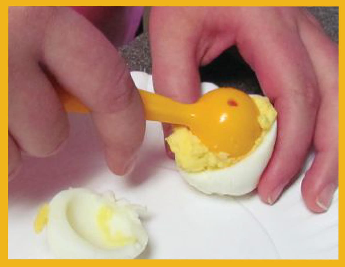 Hands scooping yolk from a hard-boiled egg with a yellow scooper.