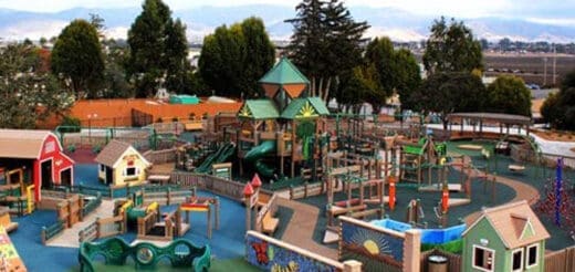 Spacious inclusive playground with colorful play structures and themed buildings.