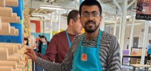Man wearing glasses and a teal apron smiles at the camera.