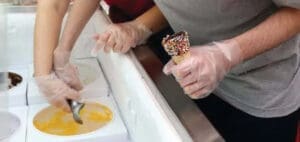 Hands in gloves scoop ice cream into a cone.
