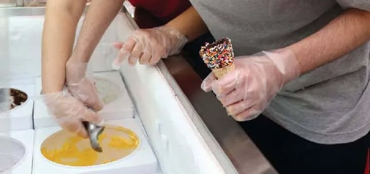 Hands in gloves scoop ice cream into a cone.