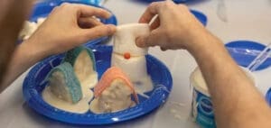 Hands assemble a mini marshmallow village on blue plates.