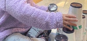 A person in a purple fuzzy sweater stacks cups.