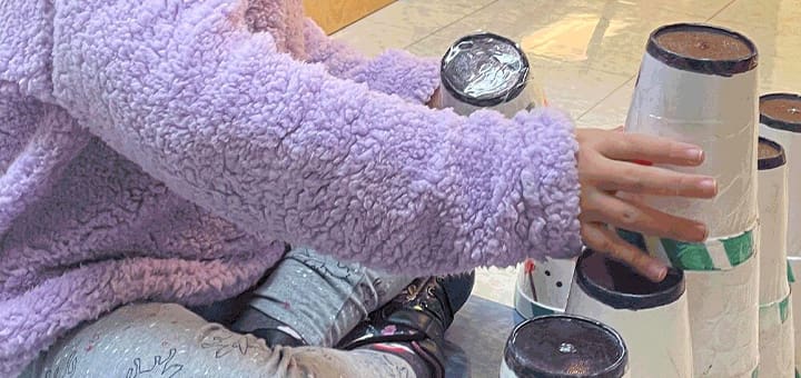 A person in a purple fuzzy sweater stacks cups.