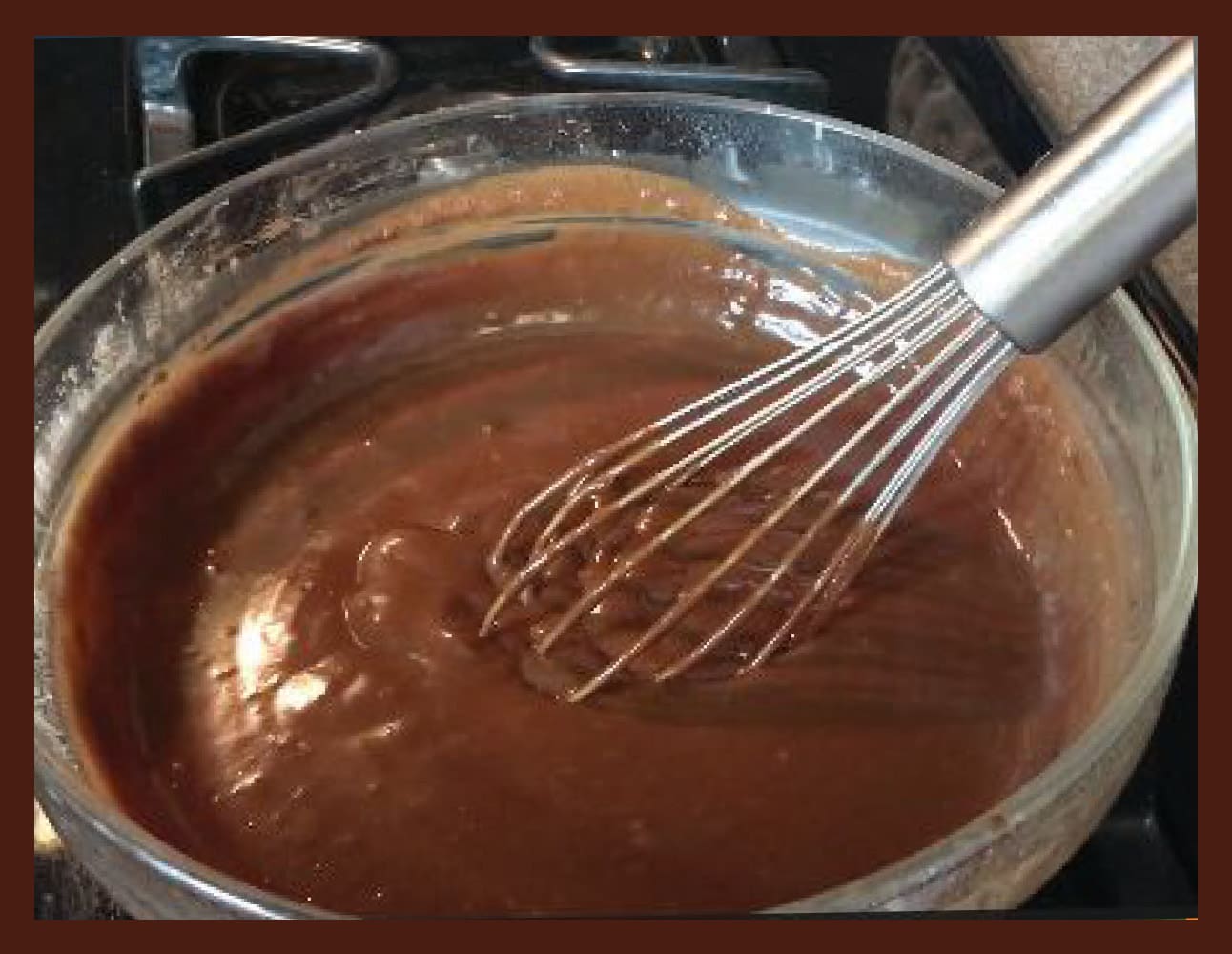 Whisk blending chocolate pudding in a glass bowl.