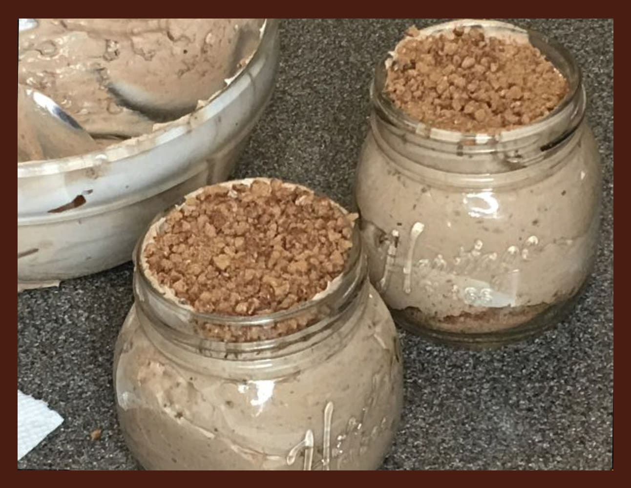 Two glass jars filled with chocolate pudding topped with crushed cookies, next to a bowl of pudding.