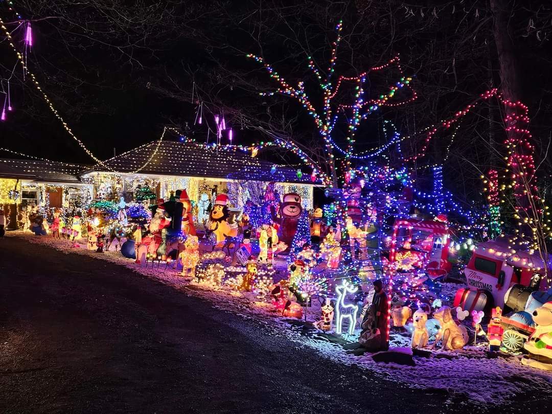 House decorated with numerous colorful holiday lights and inflatables at night.